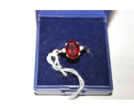 A synthetic ruby ring, the oval facet cut synthetic ruby flanked by white stones either side, on 9ct. yellow gold shank, ring