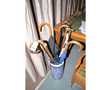 A Chinese blue and white stick stand containing a collection of walking sticks and umbrellas; and a stool.