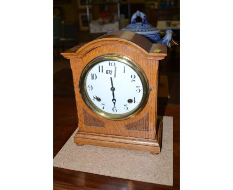 A late 19th Century mantel clock, the circular white enamel dial with arabic numerals, in arched oak case.
