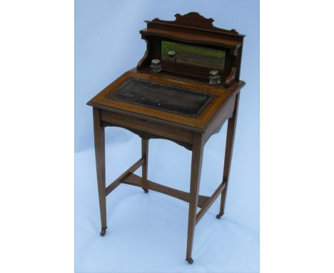 An Edwardian mahogany desk, the back fitted with a shelf over a mirror, with a pair of inkwells and pen well, the sloping ris