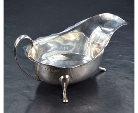 A George V silver sauce or gravy boat, with Chippendale style rim, generous spout opposed by a scrolling handle, raised on th