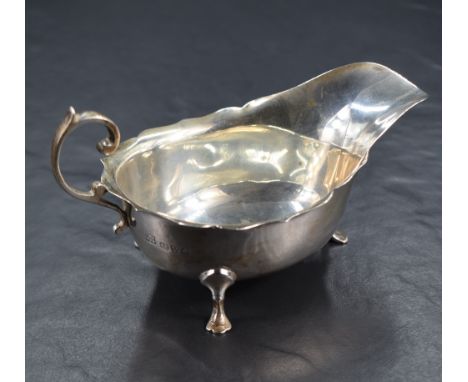 A George V silver sauce boat, with Chippendale style rim, generous spout opposed by a decorative scrolling handle, raised on 