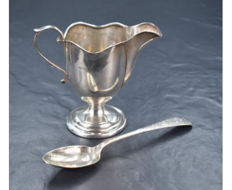 A George V silver cream jug, having a lobed rim with a narrow spout opposed by a scroll handle, raised on a circular step mou