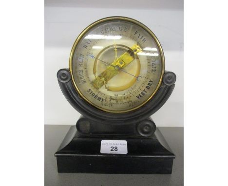 A 19th century Bourdon type barometer having a circular brass case and visible mechanism resting on an ebonized case, 8 1/2" 