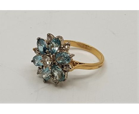 An 18ct. gold, light blue stone and diamond cluster ring. set central round brilliant cut diamond bordered by six oval cut li