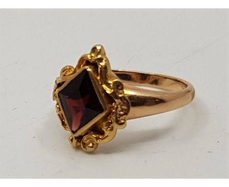 An antique precious yellow metal and garnet set ring, having scrolling mount with central lozenge cut garnet in rub over sett