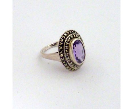 AN AMETHYST AND MARCASITE DRESS RING, with faceted central oval amethyst within two surrounds of marcasite, stamped 925, ring