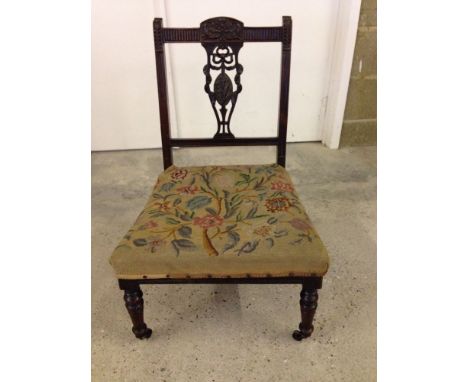 A late Victorian nursing chair with tapestry upholstered seat, fret ribbon carved back and china casters by Maples.