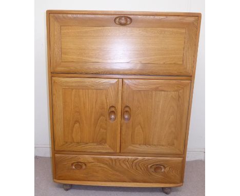 An Ercol pale coloured elm bureau with a fall front, enclosing a shelved interior, over a pair of doors and a base drawer, fi