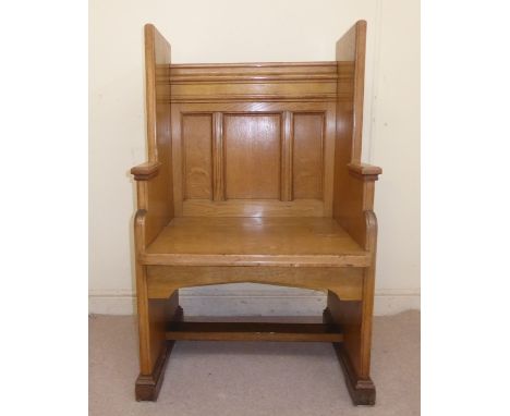 An early 20thC boarded honey coloured oak ecclesiastic's enclosed chair with a high level, tri-panelled back and solid seat, 