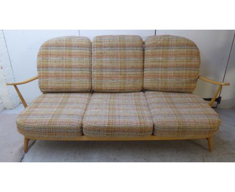 An Ercol pale coloured beech framed Windsor style settee with an angled, round, spindled back and open arms, the strapworked 