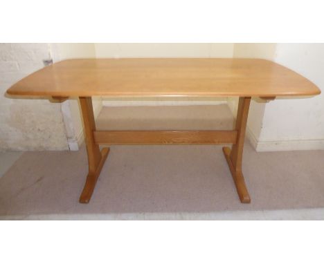 An Ercol pale coloured elm dining table, the top with round corners, raised on waisted plank trestle ends and platform feet  