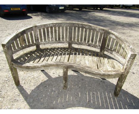 A weathered teak banana shaped garden bench, inverted serpentine seat on square cut supports, 150 cm diameter 