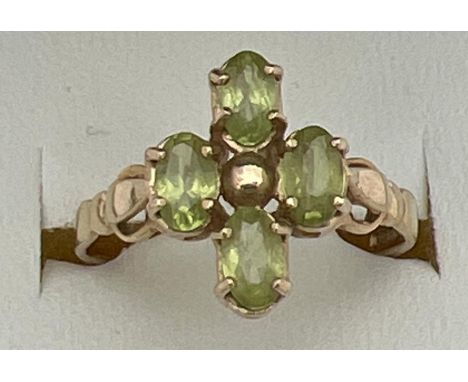 A 9ct gold and peridot ring in a quatrefoil shaped setting with shaped shoulders. 4 oval cut peridot stones, each measuring a