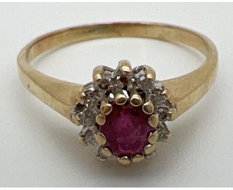 An unmarked 9ct yellow gold, ruby and diamond cluster ring in a high mount. Central oval cut ruby (approx. 5mm x 4mm) surroun