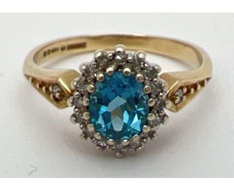 A 9ct gold, London blue topaz and diamond ring in a halo setting. Central oval cut topaz (approx. 6mm x 4mm) surrounded by a 