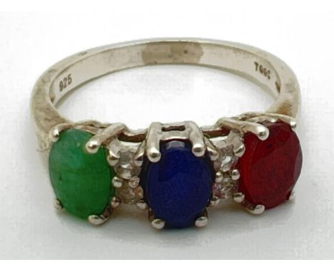 A silver trilogy dress ring set with oval cut emerald, sapphire &amp; ruby interspersed with 4 small diamonds. From The Genui