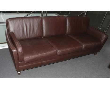 A Danish Design Three-Seater Sofa, upholstered in brown leather, with padded back support and arms, with eight cushions, on s