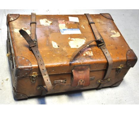 A vintage strap bound trunk with brass fittings and bearing various labels.