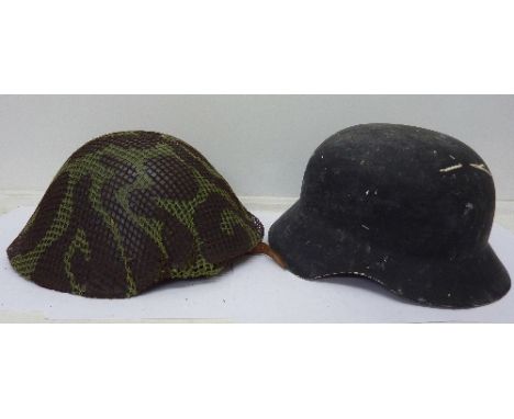 A replica composite German helmet and a British post WWII steel combat helmet with original camouflage covering