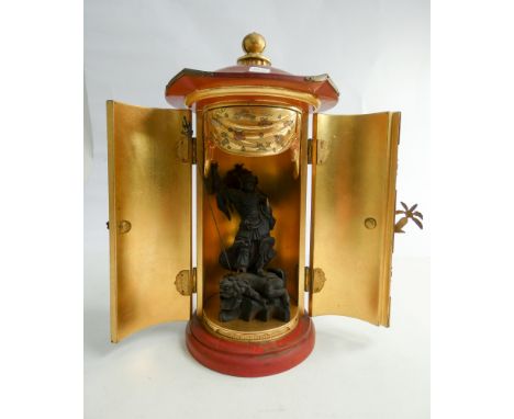 Chinese red and gilt lacquer cabinet of cylindrical form, opening to reveal carved wooden figurine of warrior astride mythica