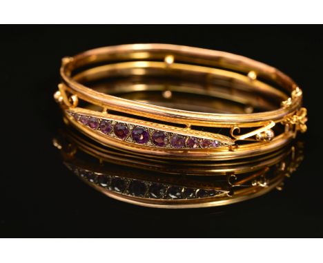 AN EARLY 20TH CENTURY 9CT GOLD AMETHYST AND DIAMOND HINGED BANGLE, designed as a navette shape panel set with a graduated lin