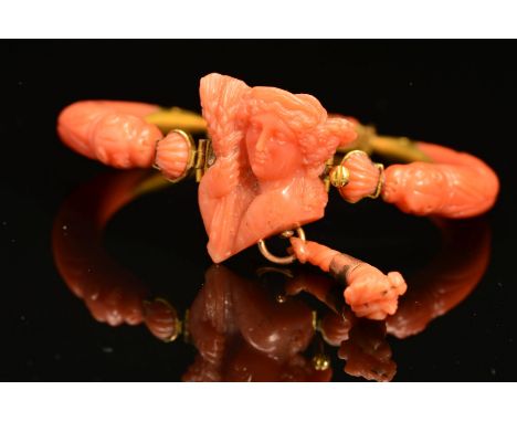 A DELICATE VICTORIAN CARVED CORAL BANGLE, centring on a carved cameo depicting Demeter, suspending a tapered coral drop, flan