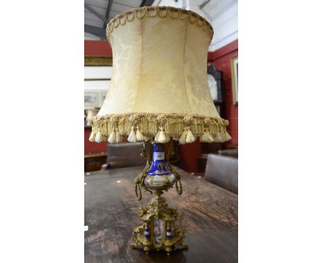 A 19th century French porcelain and ormolu table lamp, painted with a cottage view, lion mask and ring drop loop handles, gol