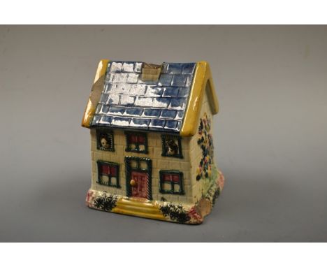 A Prattware cottage money box, with blue tiled roof, red, door, red curtains, green rope twist windows, sponged base, the sid