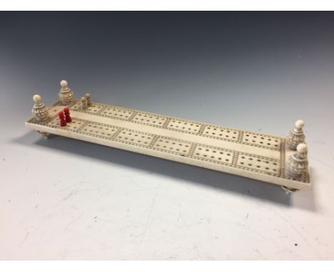 A 19th century carved ivory cribbage board, on turned supports with red stained and white pegs 28cm (11in)  