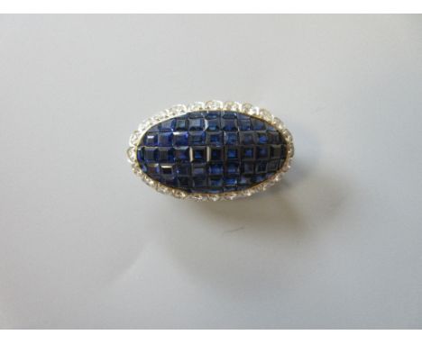 A mystery set sapphire and diamond brooch, designed as a long oval of mystery set calibré cut sapphires in a scallop edge bor