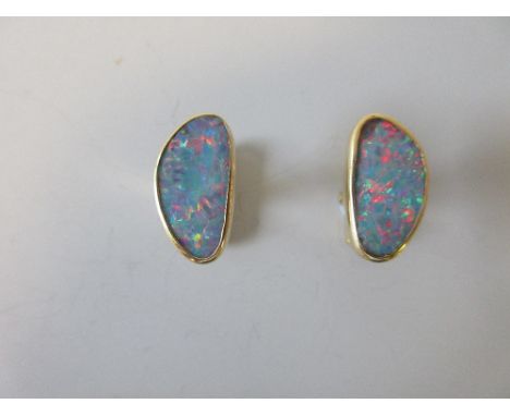 A pair of black opal cufflinks, each an asymmetric oval of flat precious opal with excellent range of colour play, predominan