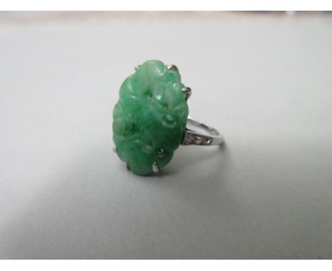 An early to mid 20th century carved jade ring with diamond shoulders, the oval green jade pierced plaque carved with fruits a