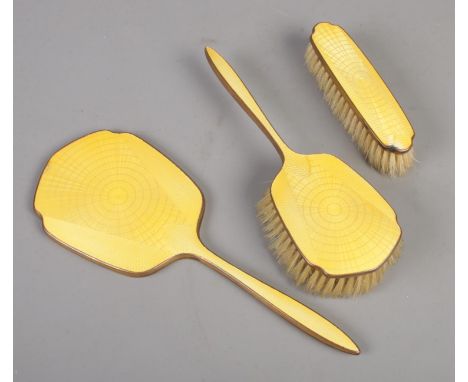 An Art Deco yellow guilloche enamel backed three piece vanity set.  Slight chips to the emamel of mirror and clothes brush.