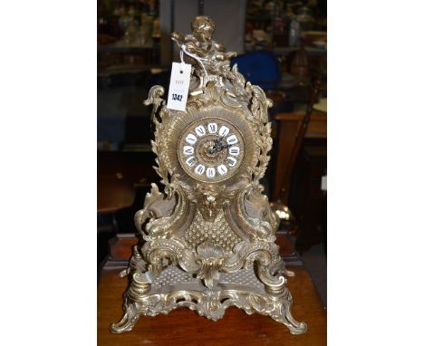 A rococo style brass mantel clock and stand, brass dial with enamel roman numerals.