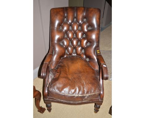 A 20th Century brown leather button back armchair with open mahogany arms, raised on brass castors.