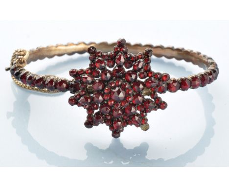 A Victorian garnet bangle, set throughout with rose cut garnets in a star pattern plaque on a single row bangle, mounted in y