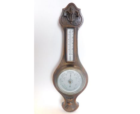A 20thC oak cased two dial barometer and thermometer, the heavily carved case with 12cm diameter barometer with a silvered di