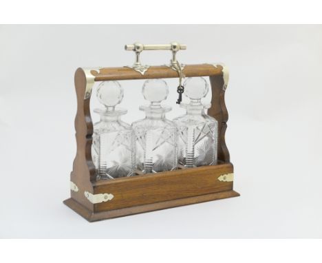 Late Victorian oak tantalus, circa 1900, having silver plated carrying handle and mounts, with key, and opening to three cut 