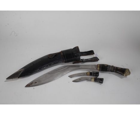 Kukri knife, to include one large and two small examples, each with horn handles and housed within a leather scabbard, 43cm l