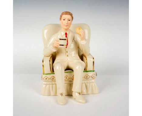 A figure of a man in white suit and pants outfit holding a cookie and a mug while seated in his white and gold trim armchair.