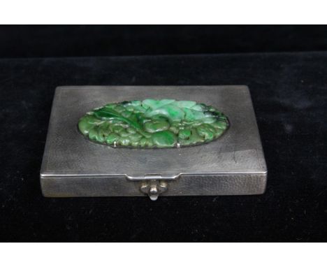 A green jade plaque, oval carved with fruiting and flowering peach branches, set on a white metal box with plannished finish,