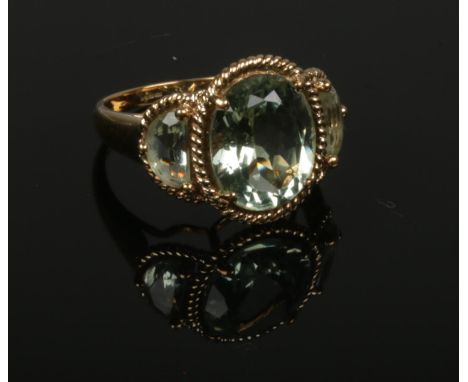 A 9ct gold three stone prasiolite dress ring set as a large ovoid stones flanked by a pair of demi lune shaped under ropetwis