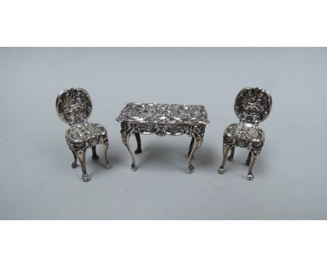 An embossed silver table and two chairs of small proportions, cherubic detail on cabriole legs, approximately 4cm tall, 20g