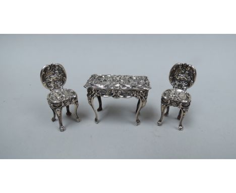 An embossed silver table and two chairs of small proportions, cherubic detail on cabriole legs, approximately 4cm tall, 20g