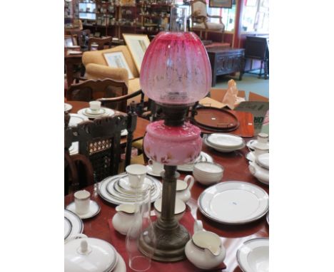 A Victorian oil lamp with cranberry shade, pink decorative reservoir and a brass base of column form, extra glass chimney 