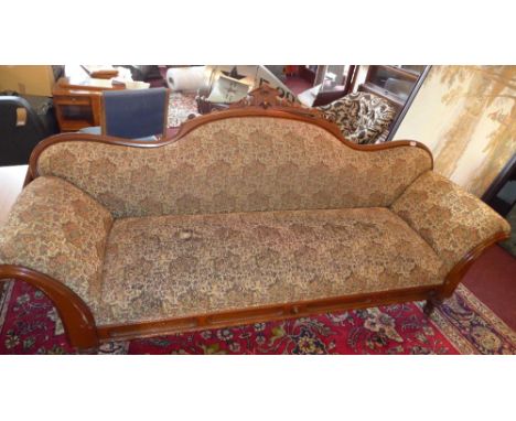 A Victorian mahogany camel back salon sofa with carved acorn crest, floral upholstery, raised on turned legs and castors.