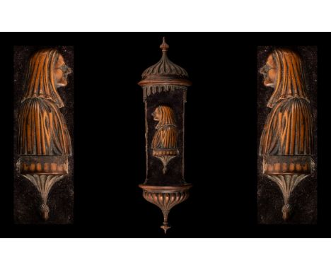 An 18th Century Holy Water Wall Bracket Carved in Fruitwood, depicting a hooded and cloaked figure in silhouette, on a purple