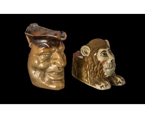 Staffordshire Pottery Sash Window Stop in the form of a roaring lion, plus a stoneware mask jug; 4 inches (10cms) high (2)