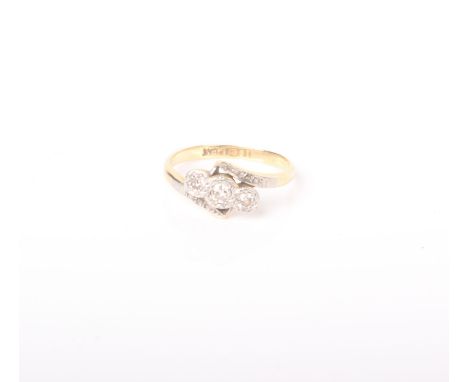 A diamond three stone cross-over ring, the graduated round brilliants illusion set in white on a yellow shank, stamped ‘18ct’